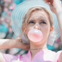 Profile headshot of blonde-haired woman blowing pink bubblegum