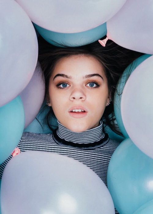 Woman with surprised expression surrounded by pink and blue balloons